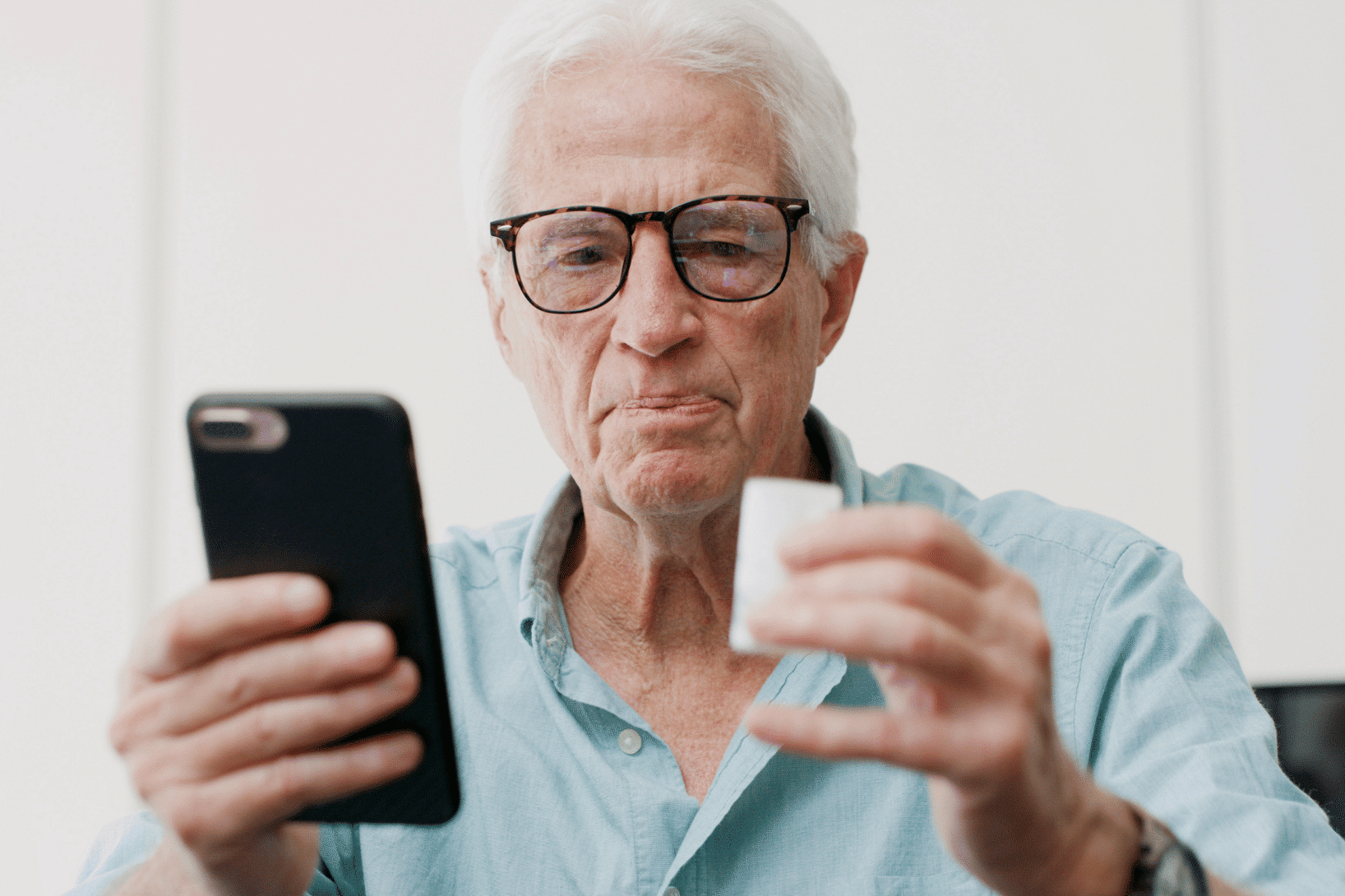 man holding pill bottle in one hand and a smartphone in the other hand